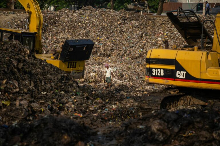 Excavators working at a large landfill with a person managing waste disposal operations.