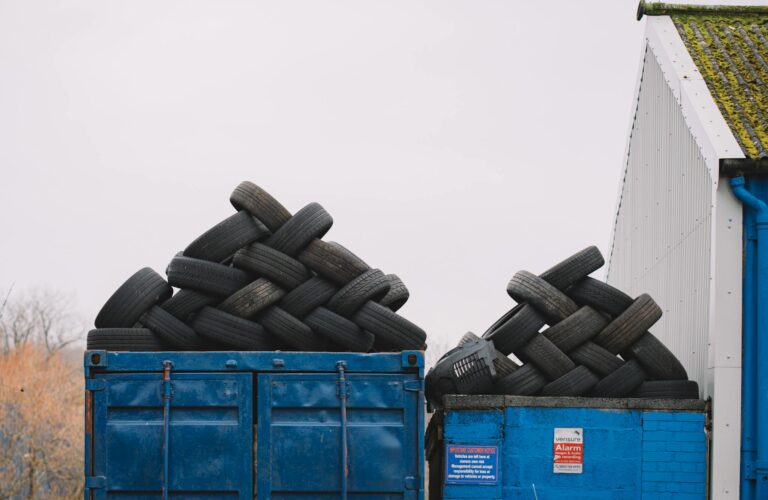 Piles of used tires on blue containers in an industrial recycling yard.