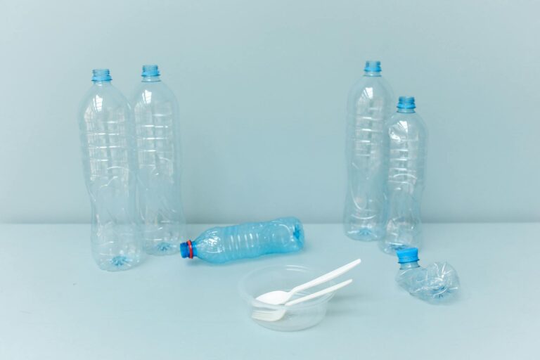 Plastic bottles and disposable utensils on a minimalist blue background, highlighting waste.